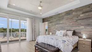 A bedroom with a large bed, a bench, a nightstand, and a view of the outdoors. - Heaven Found!  Stunning River Views & Pool - Villa Island Sunset - Roelens Vacations (Fort Myers)