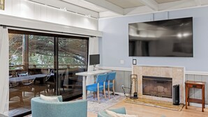 Uma sala de estar moderna com lareira, uma televisão grande fixada na parede e um espaço de refeições com vista para o exterior.