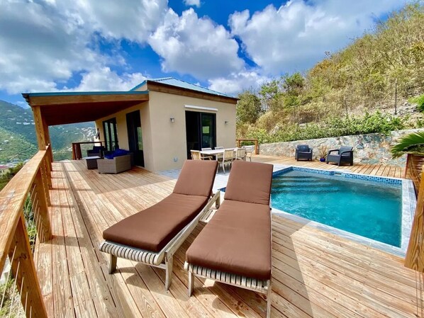 A wooden deck with two lounge chairs and a small pool.