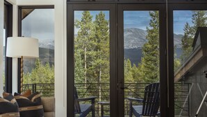 Ein Balkon mit Blick auf einen Wald und Berge. Zwei Stühle und ein Tisch befinden sich auf dem Balkon.