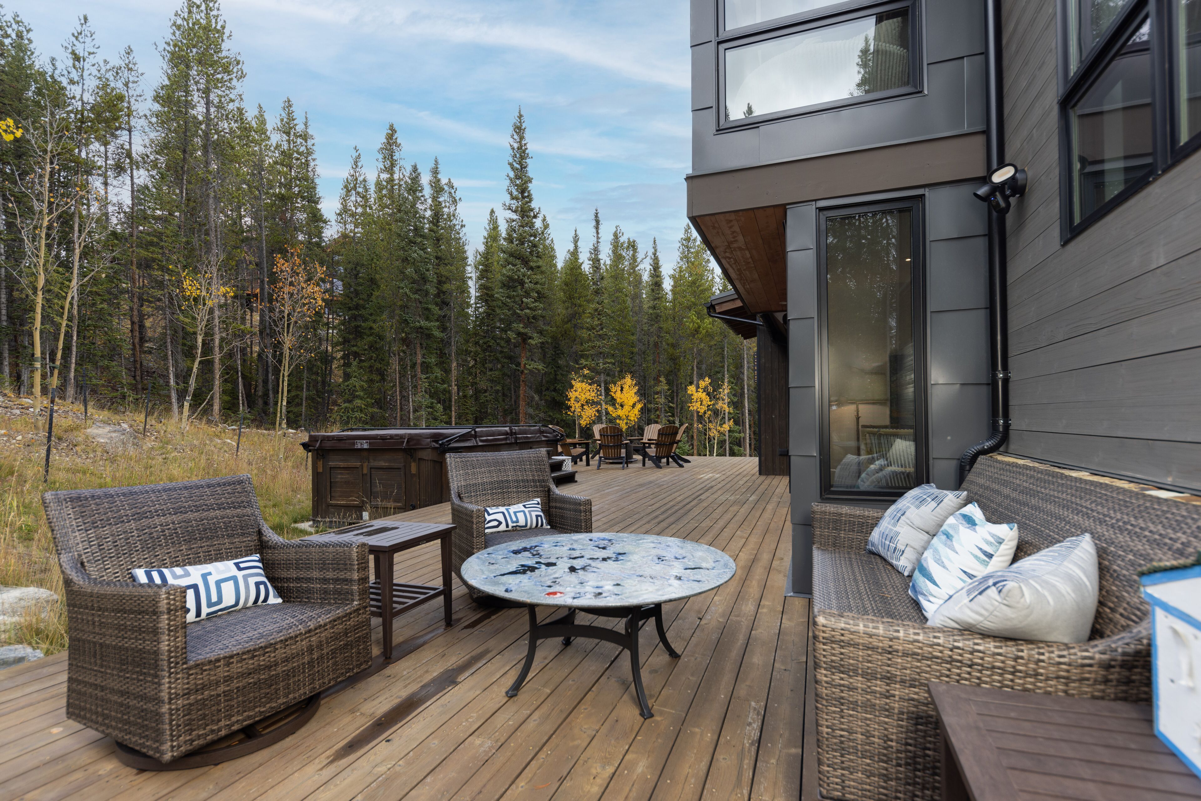 Une terrasse dotée de meubles en osier, d’une table ronde et offrant une vue sur une forêt.