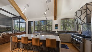 Eine moderne Küche mit einer großen Kochinsel, Barhocker und Blick auf den Wald durch große Fenster.