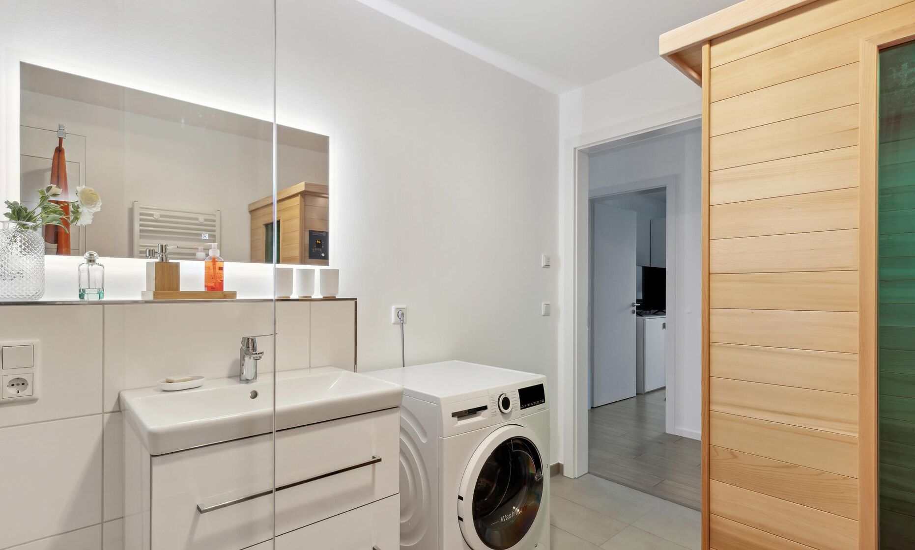 A modern bathroom with a sink, mirror, and washing machine.