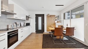 Eine moderne Küche mit weißen Schränken, einem Einbauofen und einem Essbereich mit einem Holztisch und Stühlen.