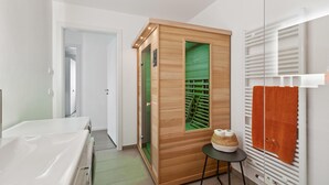 Ein modernes Badezimmer mit einer hölzernen Sauna, einer weißen Badewanne und einem Handtuchhalter mit einem orangefarbenen Handtuch.
