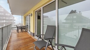 Ein Balkon mit Holzboden, Metallstühlen und einem Tisch.