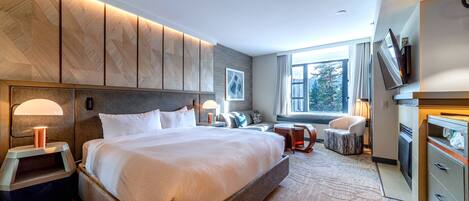 A modern hotel room with a large bed, bedside lamps, a flat-screen TV, a desk, and a view of the outdoors.