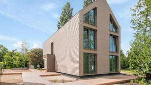 Una casa moderna de dos pisos con techo inclinado, ventanas amplias y un patio pavimentado.