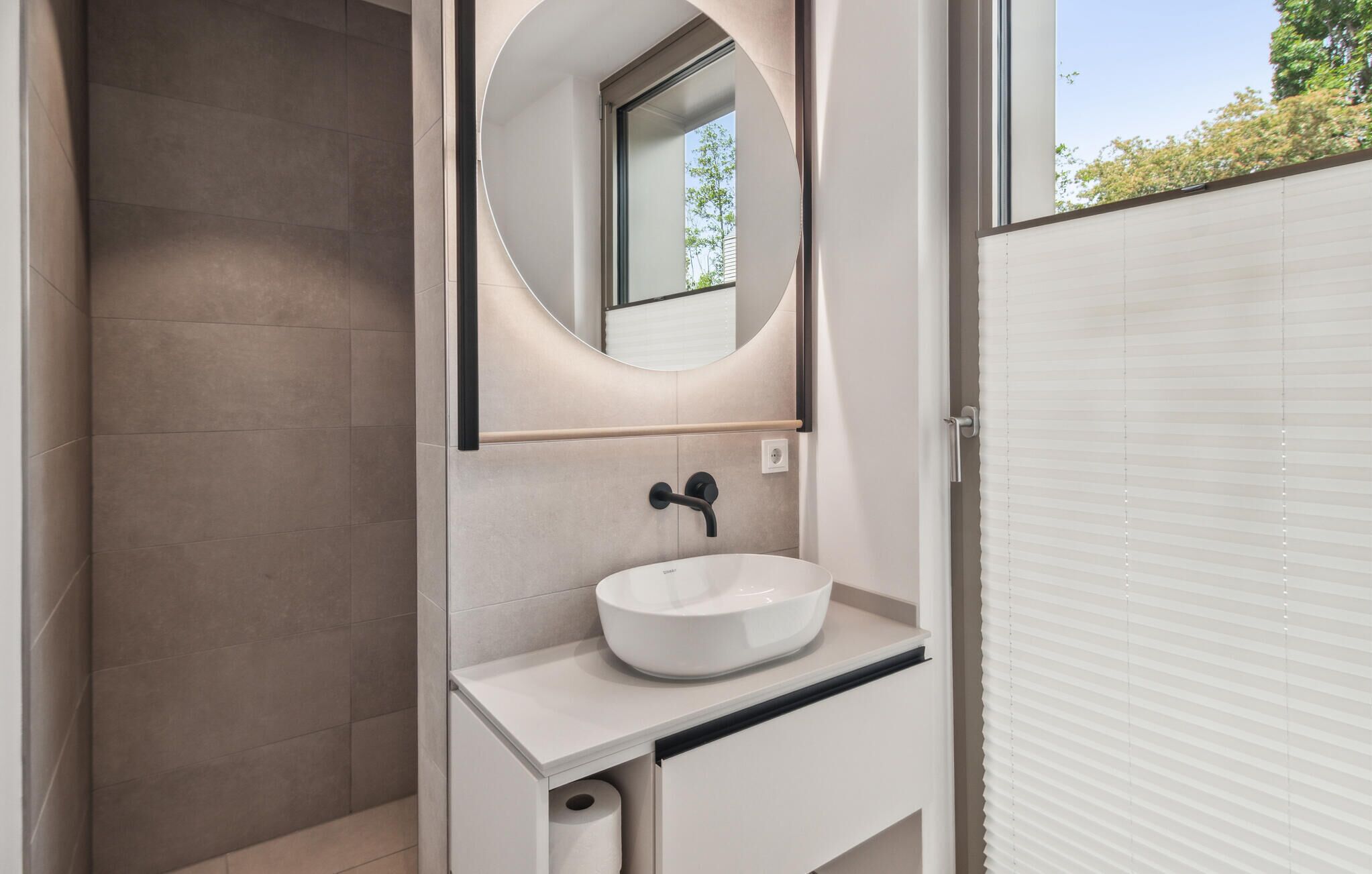 A modern bathroom with a white sink, a round mirror, and a shower area.