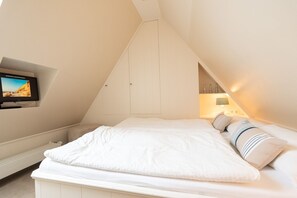 Ein Schlafzimmer mit Bett, Wandfernseher und schrägen Wänden.