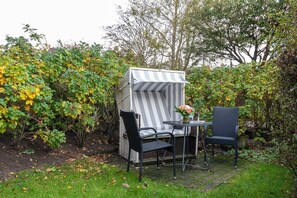 Ein kleiner Sitzbereich im Freien mit einem Streifen-Markisenvorzelt, zwei Stühlen und einem Tisch mit Blumen in einer Vase.