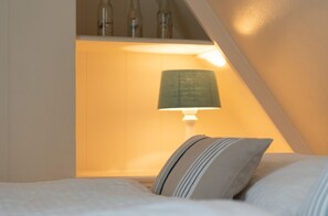 A bedroom with a bed, a bedside lamp, and a shelf with bottles.
