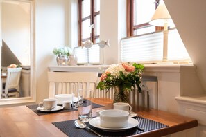 Ein Esstisch gedeckt mit weißem Geschirr, Gläsern und einer Blumenvase.