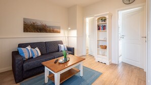 A living room with a dark grey sofa, a wooden coffee table, a blue rug, a bookshelf, and a white door.