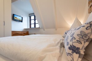 Un dormitorio con una cama, un aparador, una ventana y un televisor en la pared.