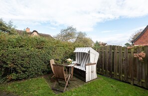 A patio with a table and chairs, surrounded by a wooden fence and dense greenery.