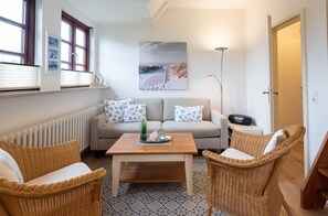 Ein gemütliches Wohnzimmer mit einer Couch, zwei Korbstühlen, einem Couchtisch und einer Stehlampe.