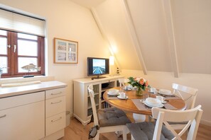 Un comedor acogedor con una mesa de madera dispuesta para dos personas, un televisor sobre un escritorio y una ventana con persianas.
