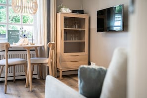 A modern living room with a wooden cabinet, a TV mounted on the wall, and a dining area with a table and chairs.