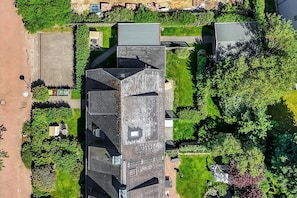 An aerial view of a building with a sloped roof, surrounded by greenery and a paved area.