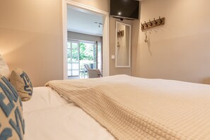 Ein Schlafzimmer mit einem großen Bett, einem an der Wand montierten Fernseher und einer Tür, die auf einen Balkon führt.
