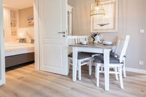 Ein Zimmer mit einem Bett, einem Esstisch mit Stühlen, einer weißen Tür und einer Wandleuchte.