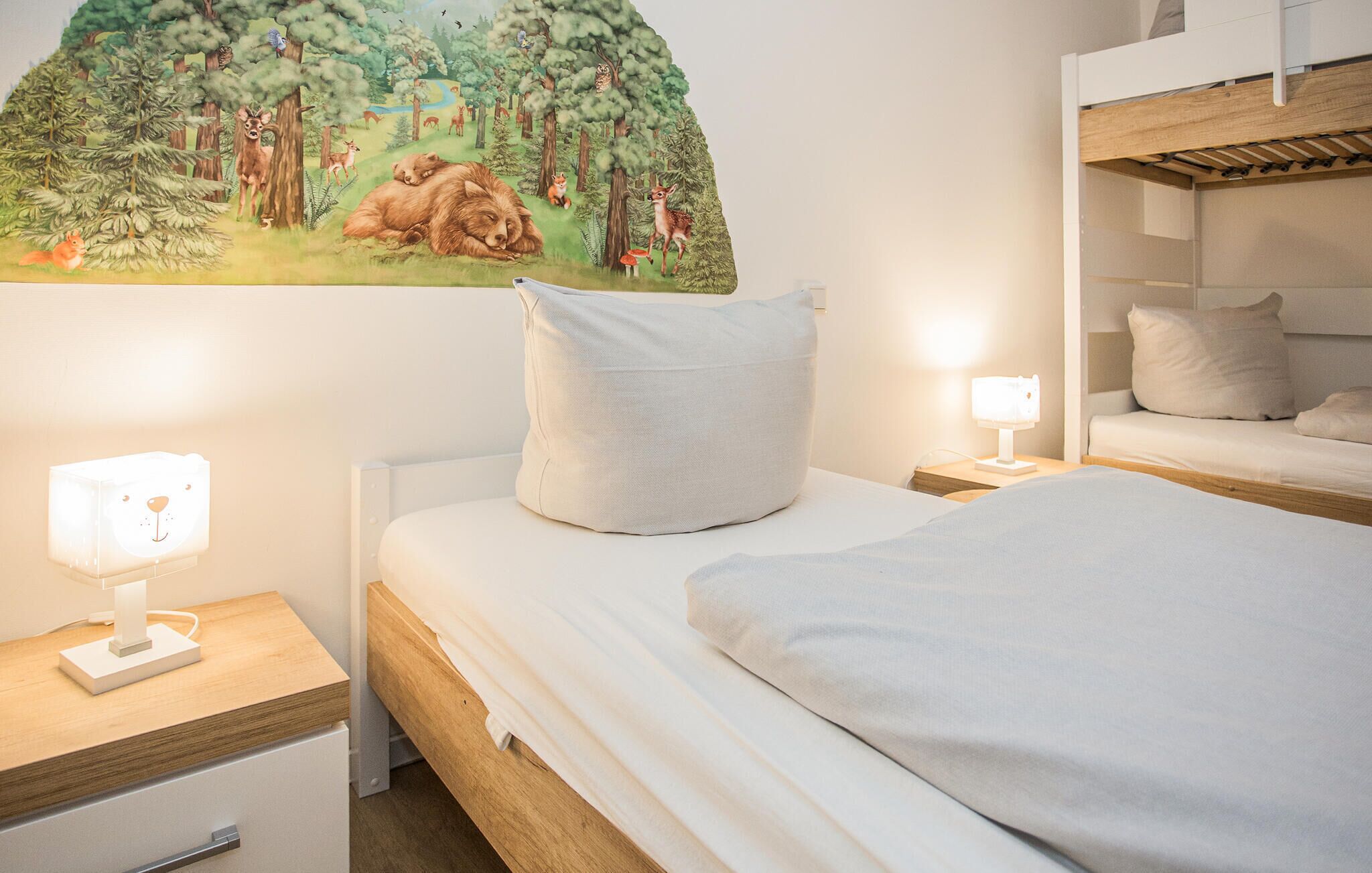 Een slaapkamer met een bed, nachtkastje, lamp, wandplank en een stapelbed.