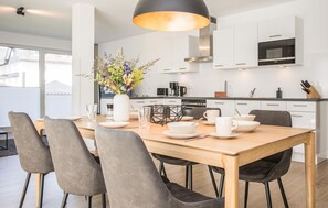 A modern kitchen with white cabinets, a dining table with chairs, and a vase with flowers.