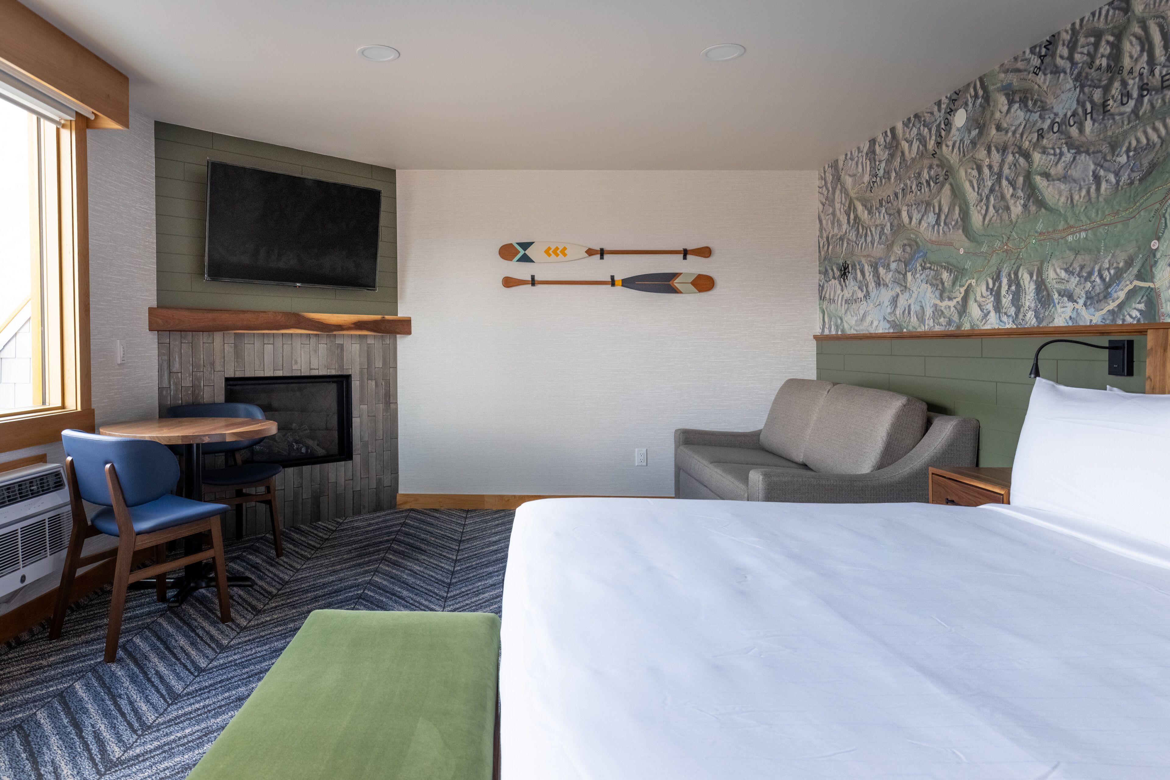 Una habitación de hotel con cama, escritorio, sillón, sofá, chimenea y un mapa mural.