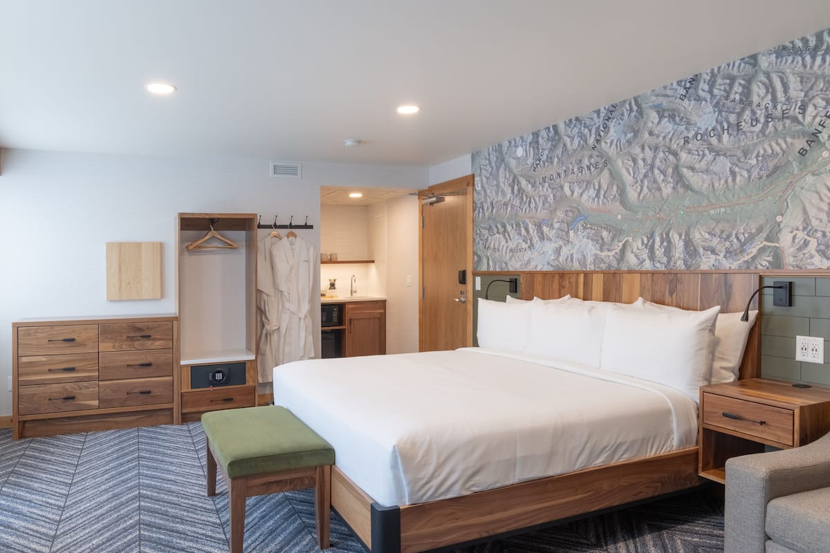 A modern hotel room with a large bed, wooden furniture, a map on the wall, and a small seating area.
