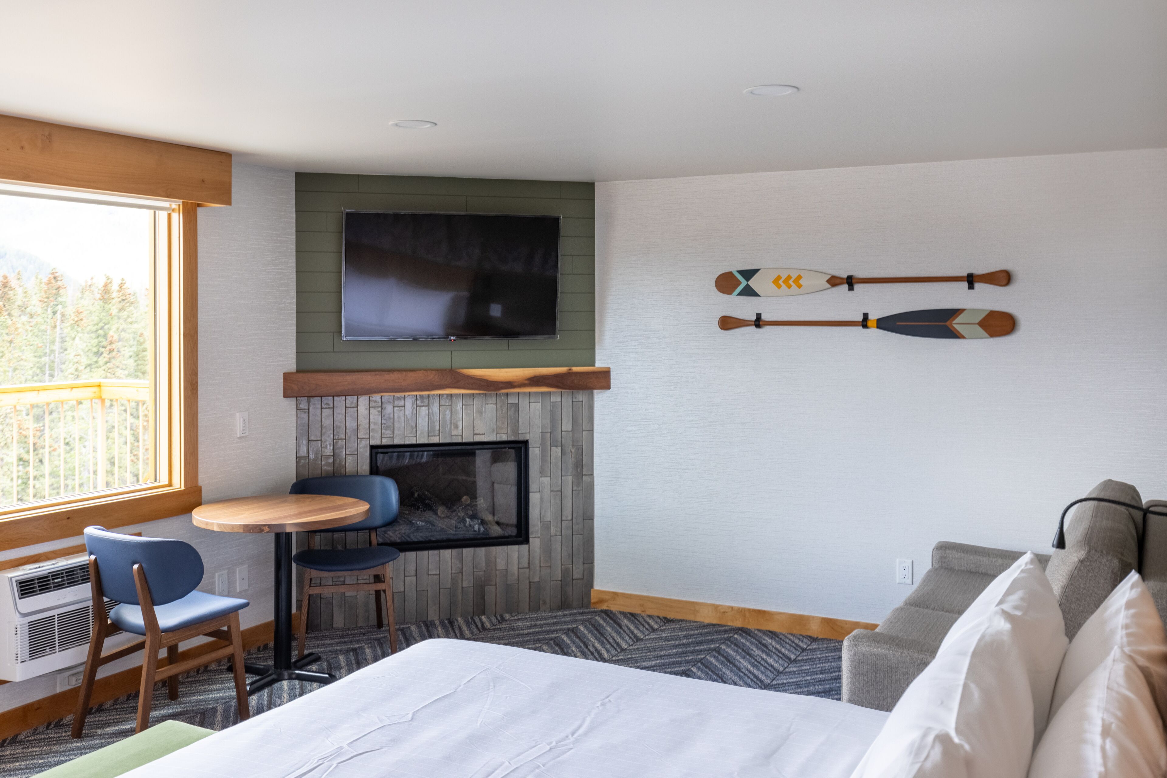 Une chambre d’hôtel avec un lit, un téléviseur fixé au mur, une cheminée et deux tableaux représentant des bateaux à rames.