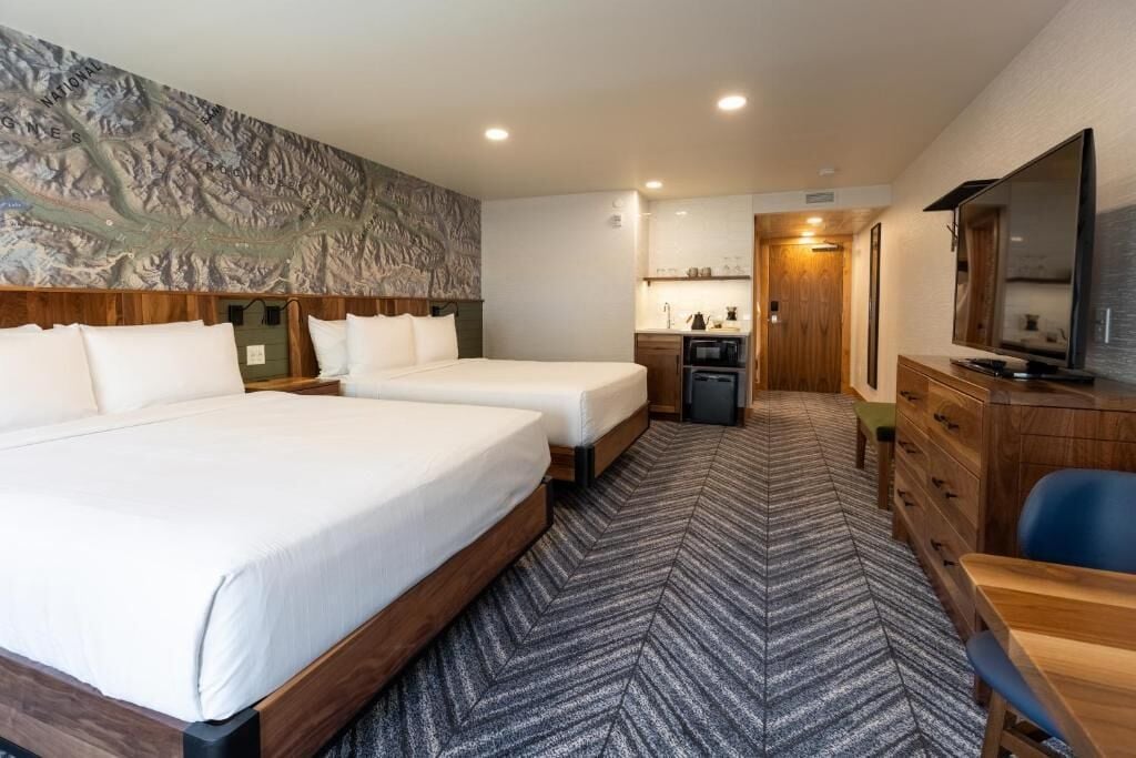 A hotel room with two beds, a kitchenette, a television, and a large mirror.