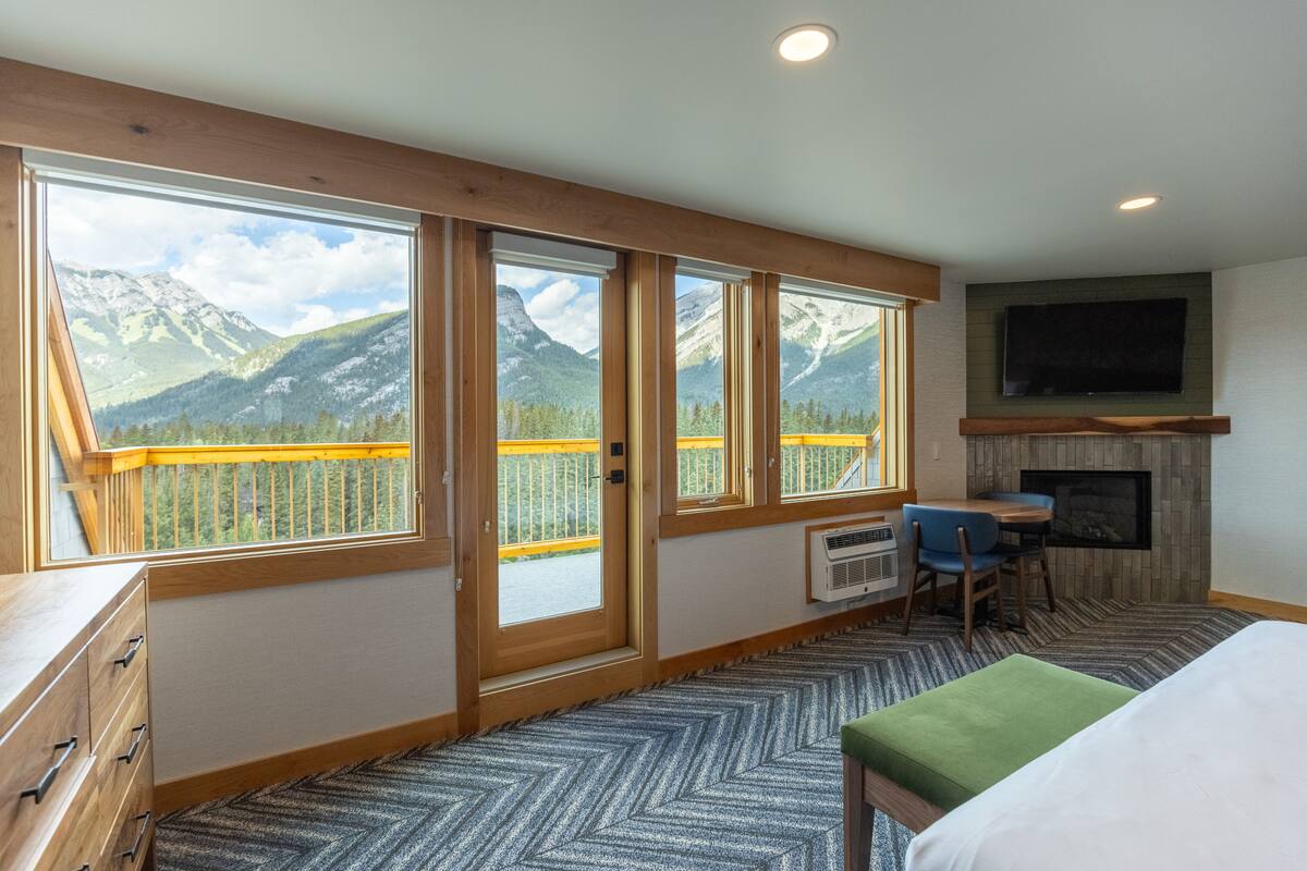 A room with large windows offering mountain views, a fireplace, a television, and a dining area.