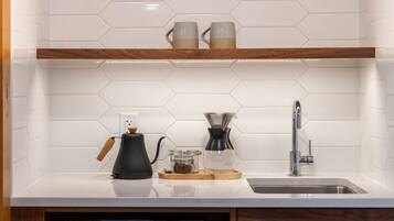 A kitchen with a white countertop, a coffee maker, a glass carafe, and a sink.