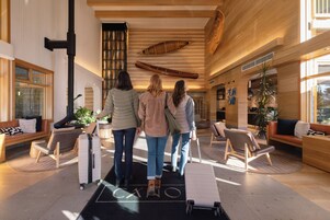 A spacious lobby with a high ceiling, wooden beams, and a large canoe hanging on the wall. There are several seating areas with modern furniture and a large window providing natural light.