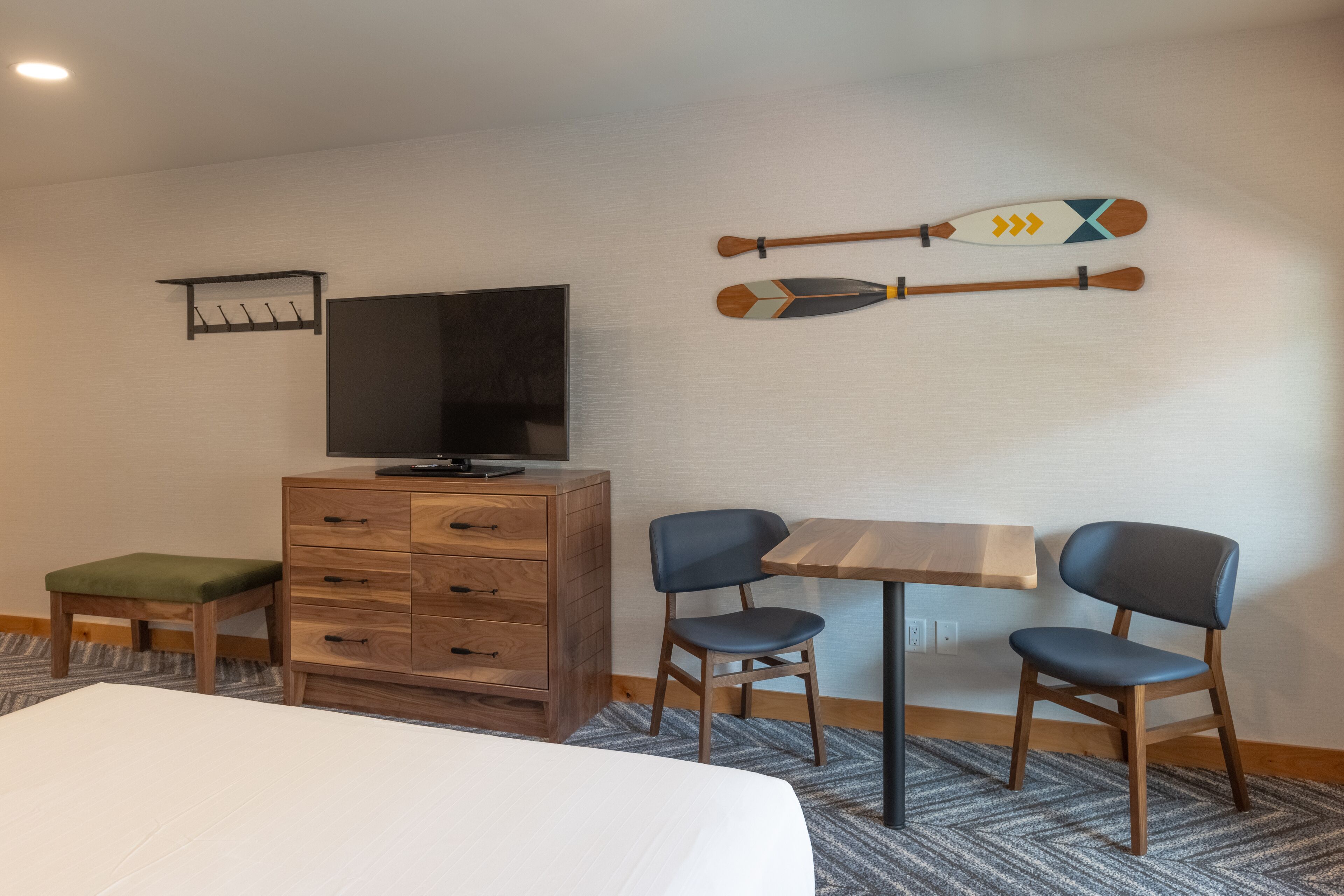 Ein Hotelzimmer mit einem Bett, einem Holzschrank, einem Fernseher, zwei Sesseln und einem Tisch.