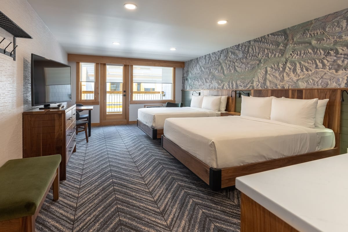 A hotel room with two beds, a desk, a television, and a large window.