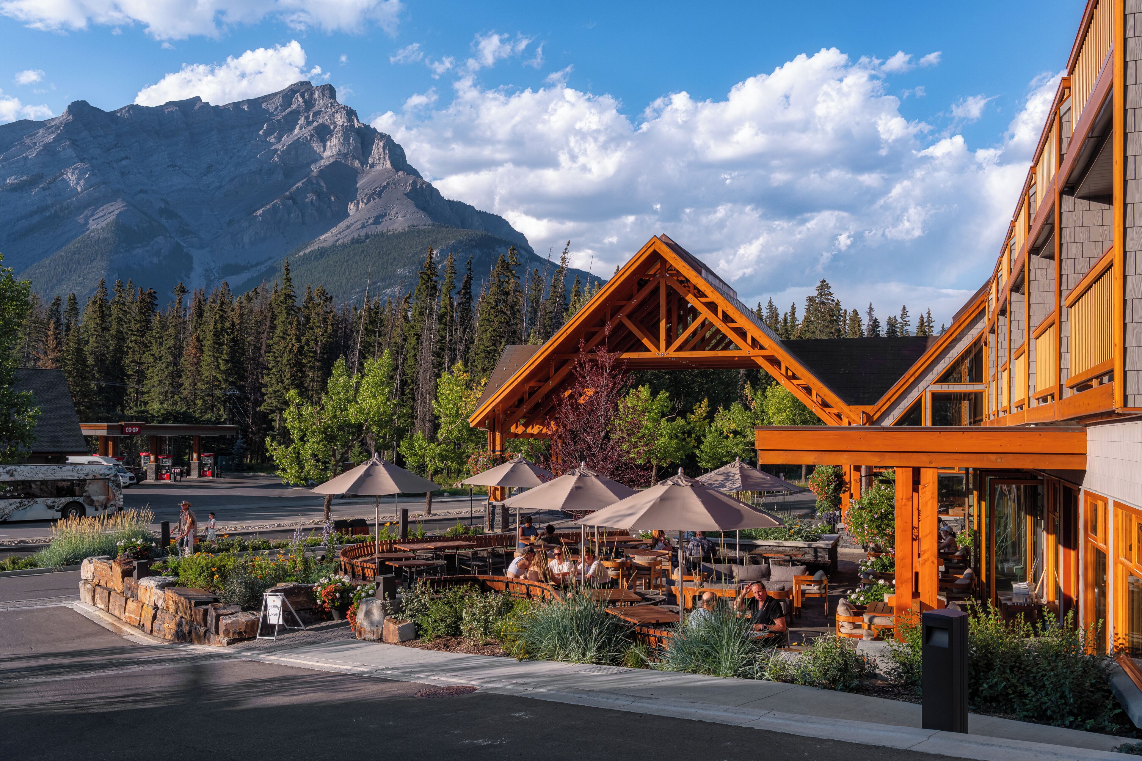 A restaurant with outdoor seating, a mountain backdrop, and a modern building with wooden architecture.