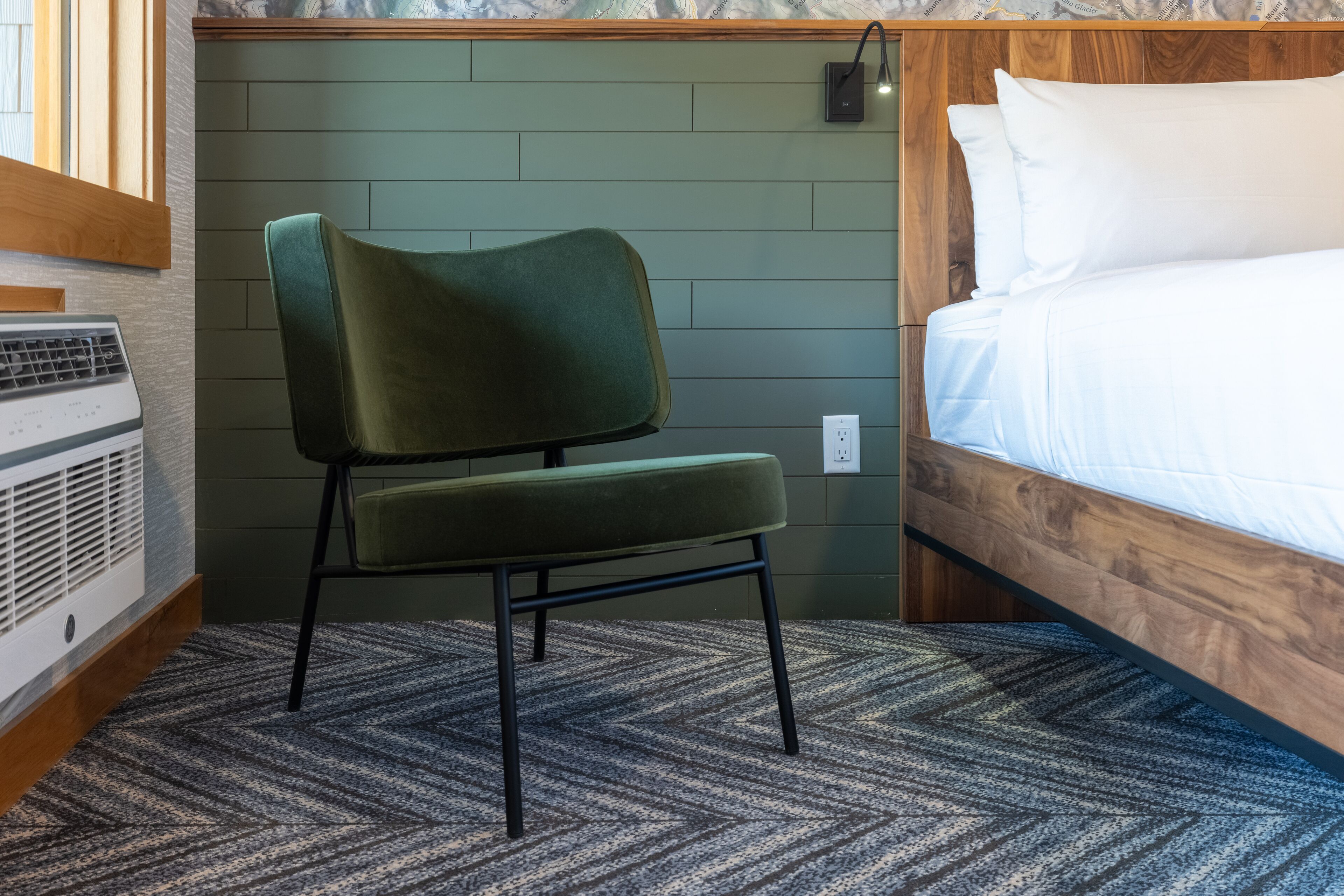 A room with a bed, a green upholstered chair, a heater, and a patterned carpet.