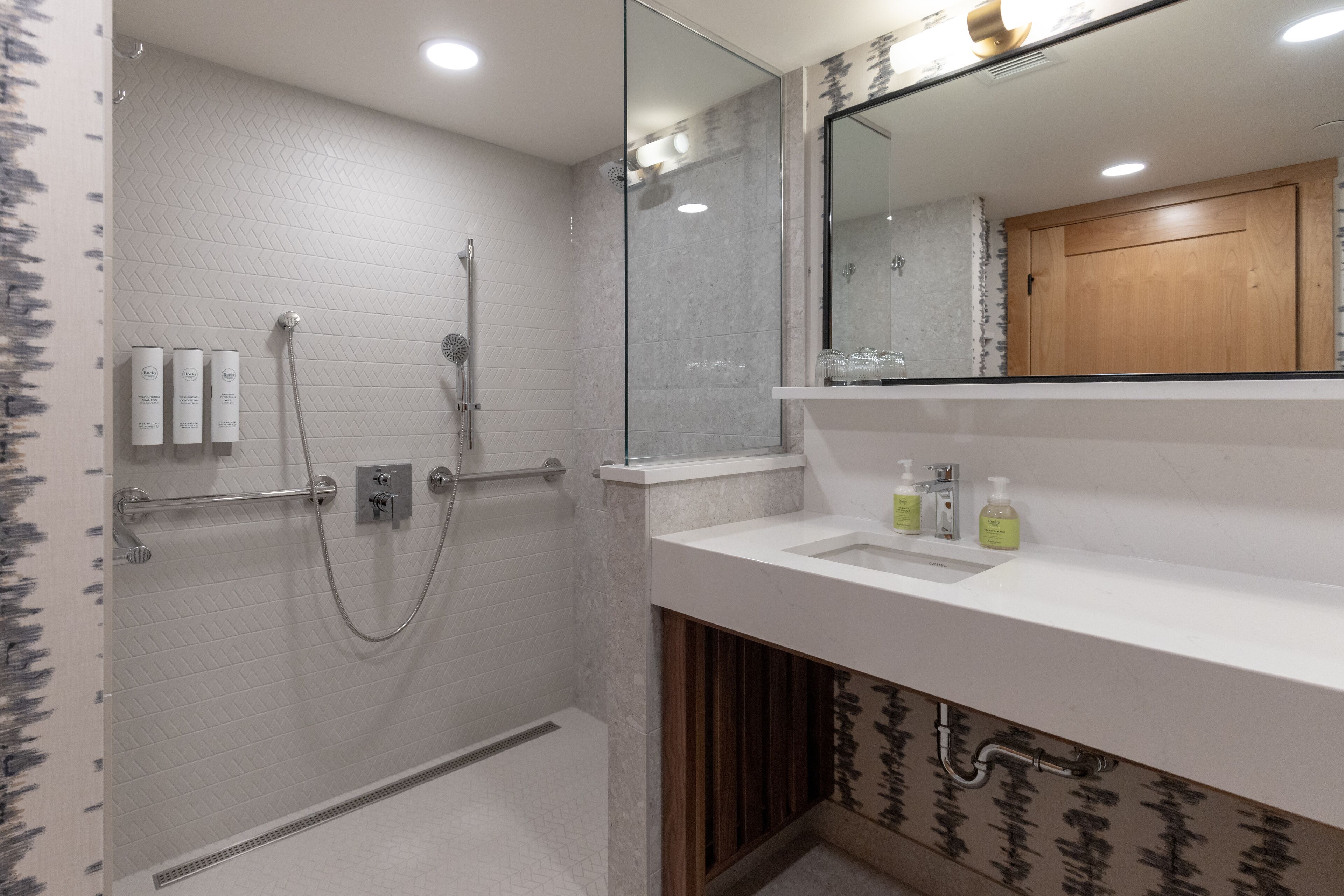 Un bagno moderno con box doccia in vetro, un lavabo bianco con articoli da toilette e un armadietto in legno.