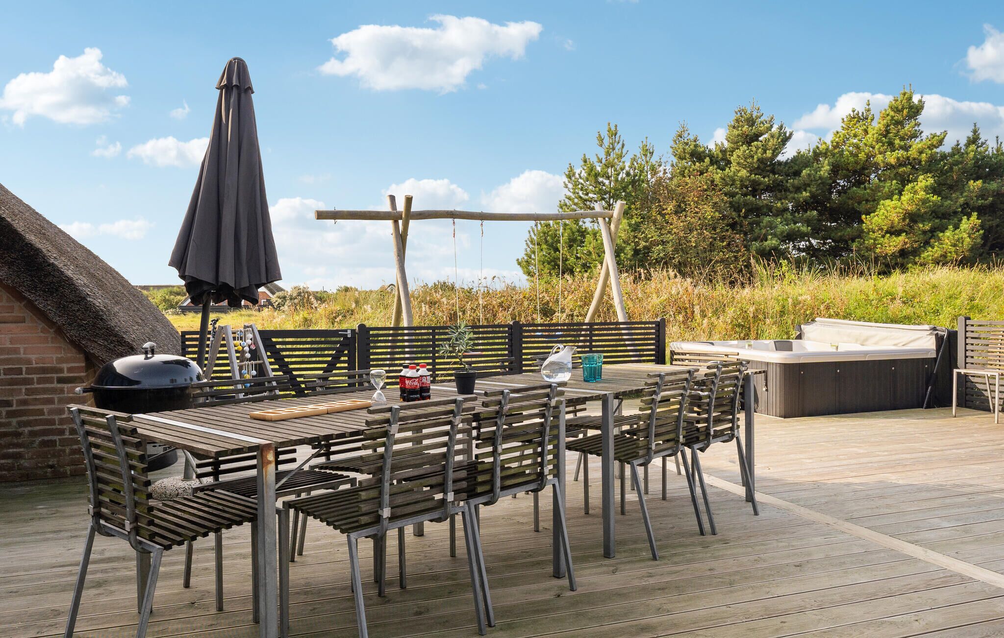 En träveranda med ett bord och stolar, en grill, ett bubbelbad och en gunga.