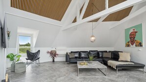 Ein geräumiger Wohnbereich mit einer schwarzen Ledersofa, einem Couchtisch und einem schwarzen Sessel. An der Wand hängt ein Gemälde und auf dem Boden steht eine Pflanze.