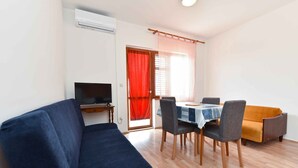 A living room with a sofa, a dining table with chairs, a TV, and a window with curtains.