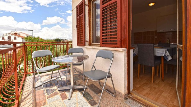 A balcony with a table and chairs, a view of a building, and a kitchen area visible through an open door.
