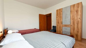 A bedroom with two beds, a wooden wardrobe, and a nightstand with a lamp.