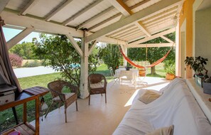 Relax in a serene outdoor space surrounded by lush greenery, featuring a comfortable sofa and wicker chairs.