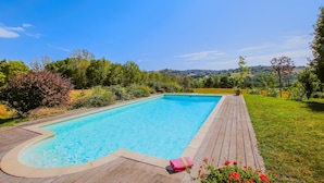 A rectangular swimming pool with a wooden deck, surrounded by lush greenery and a clear view of distant hills. - Stunning home in Monseveroux (Monseveroux)