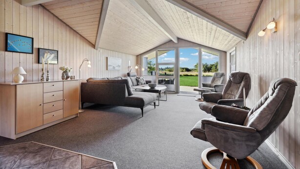 Amplia habitación con techo alto, un sofá, dos sillones, una mesita y un armario. Amplias ventanas ofrecen vistas al exterior.
