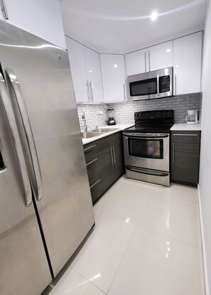 Una cocina moderna con electrodomésticos de acero inoxidable, armarios blancos y un salpicadero de azulejos.