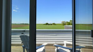 A balcony with two white Adirondack chairs and a view of a green field and trees. - Gorgeous home in Tossens with sauna (Tossens)